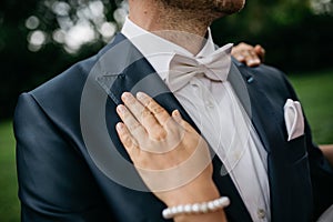 The hand of a bride on the handsome young groom in a classic black suit