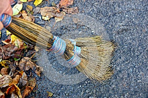 Hand with a broom sweeps dry leaves from the asphalt