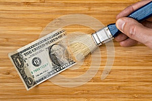 Hand with a brush painting one dollar bill on the wooden background