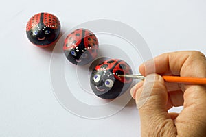 Hand with brush painting three stones as ladybugs