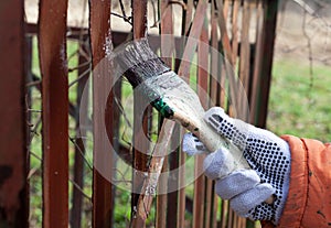 A hand with a brush paints an old fence in the garden