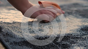 Hand-brushed carpet close-up. A hand with an orange brush rubs the surface of the carpet on the street. Slow motion