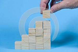 Hand is building stair steps from blank wooden cubes, business growth and management success concept, blue background with copy