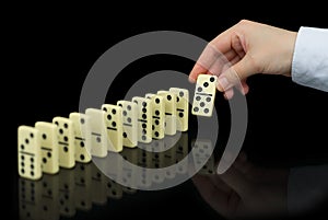 Hand builds a line of dominoes on black background