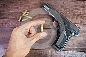 Hand with bullet and Semi-automatic 9mm gun on wooden background