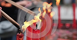 Hand burning incense stick on red candle fire in temple