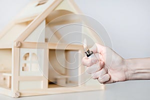 Hand with burning lighter against wooden house model on the background. Arson of house concept. Criminal accident
