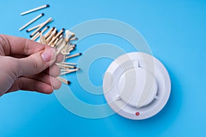 Hand with a burning match and a fire detector on a blue background. Fire safety concept