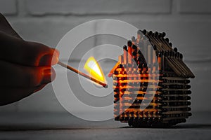 Hand with a burning match sets fire to the house model of matches, risk, property Insurance protection or ignition of combustible