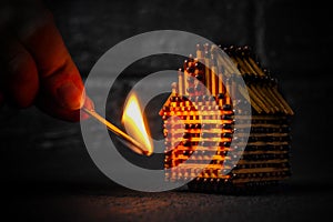 Hand with a burning match sets fire to the house model of matches, risk, property Insurance protection or ignition of combustible