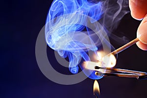 Hand and burning matchsticks with smoke spreading on blue background