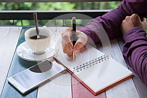 hand of business man holding pen writing on notebook paper. front of him have coffee cup with coffee and smartphone putting on