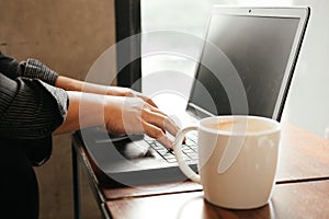 hand of business man typing on keyboard computer notebook. coffee cup putting beside laptop on wooden table. image for technology