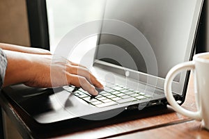 hand of business man typing on keyboard computer notebook. coffee cup putting beside laptop on wooden table. image for technology