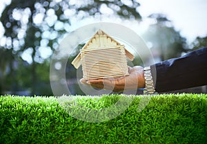 hand of business man and wood house model on beautiful green grass field use for housing ,residental real estate and land