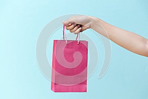 Hand of business woman hold pink shopping bag on blue concrete