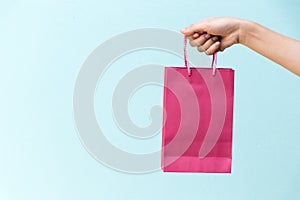 Hand of business woman hold pink shopping bag on blue concrete b