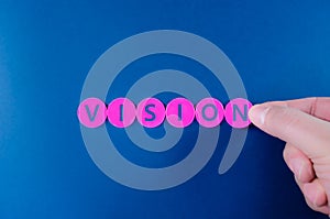 Hand of a businessman adding the last letter to spell word vision on pink circles