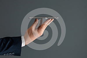 The hand of a businessman in a business suit holds a smartphone horizontally side view. Close-up