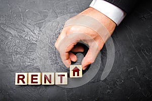 The hand of a businessman in a business suit stretches a cube with a picture of a house to the word rent. The concept of renting