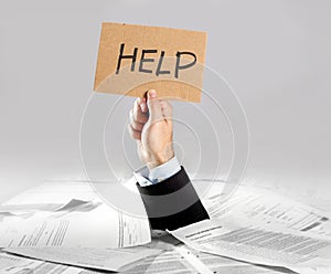 Hand of businessman emerging from loaded paperwork desk holding help message