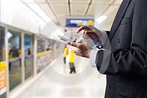 Hand of Businessman hold Wireless Digital Smart Device or Smartphone while waiting for Subway Train