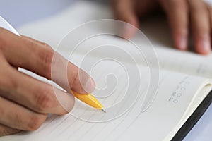 Hand of businessman hold a yellow pen writing to the note on pap