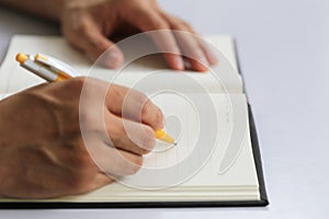 Hand of businessman hold a yellow pen writing to the note on pap