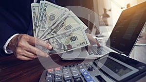 Hand of businessman holding banknotes and using calculator and laptop calculating finance and turnover at office work