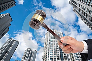 Hand of a businessman holding a judge gavel on the building background. Auction or bankruptcy concept.