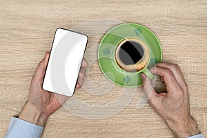 Hand of businessman holding mobile phone with white screen while drinking black coffee