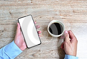 Hand of businessman holding mobile phone with white screen while drinking black coffee cup on table