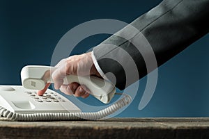 Hand of a businessman holding telephone handset dialing phone number