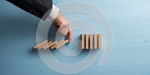 Hand of a businessman interrupting collapsing dominos with his finger