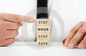 Hand of a businessman pointing at stack of wooden blocks with sign Stay Home Stay Safe