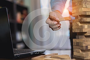 Hand of businessman pulling wooden block before fail on building tower