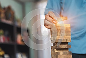 Hand of businessman pulling wooden block before fail on building tower at home