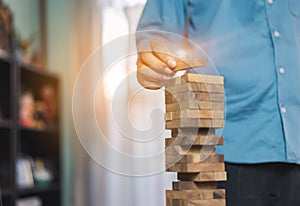 Hand of businessman pulling wooden block before fail on building tower at home