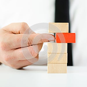 Hand of a businessman pushing red wooden block out of stack of blocks