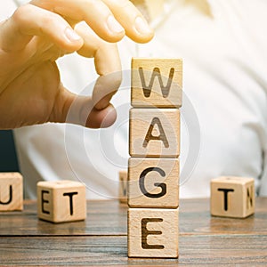 Hand of a businessman removes wooden blocks with the word Wage. Salary reduction concept. Wages cuts. The concept of limited