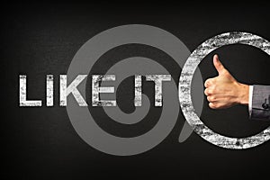 Hand of a businessman showing thumbs up for the phrase LIKE IT written on a blackboard