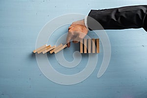 Hand of a businessman stopping collapsing dominos in a conceptual image of crisis management