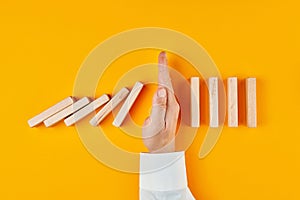 Hand of a businessman stopping domino effect on yellow background