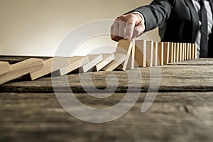 Hand of businessman stopping falling domino pieces