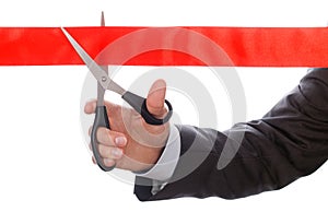 Hand of businessman in suit cutting red ribbon with pair of scis