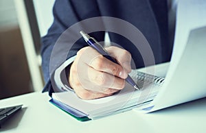 Hand of businessman in suit filling and signing with blue pen partnership agreement form clipped to pad closeup