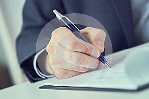 Hand of businessman in suit filling and signing with blue pen partnership agreement form clipped to pad closeup