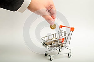 The hand of a businessman in a suit puts a coin in a trolley with money. The concept of capital accumulation, increasing profits.