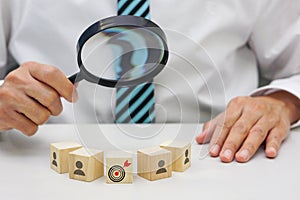 Hand of businessperson looking at wooden blocks with various icon symbols through magnifying glass.