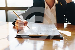 Hand of businesswoman sitting at the table and writing on business contract in office